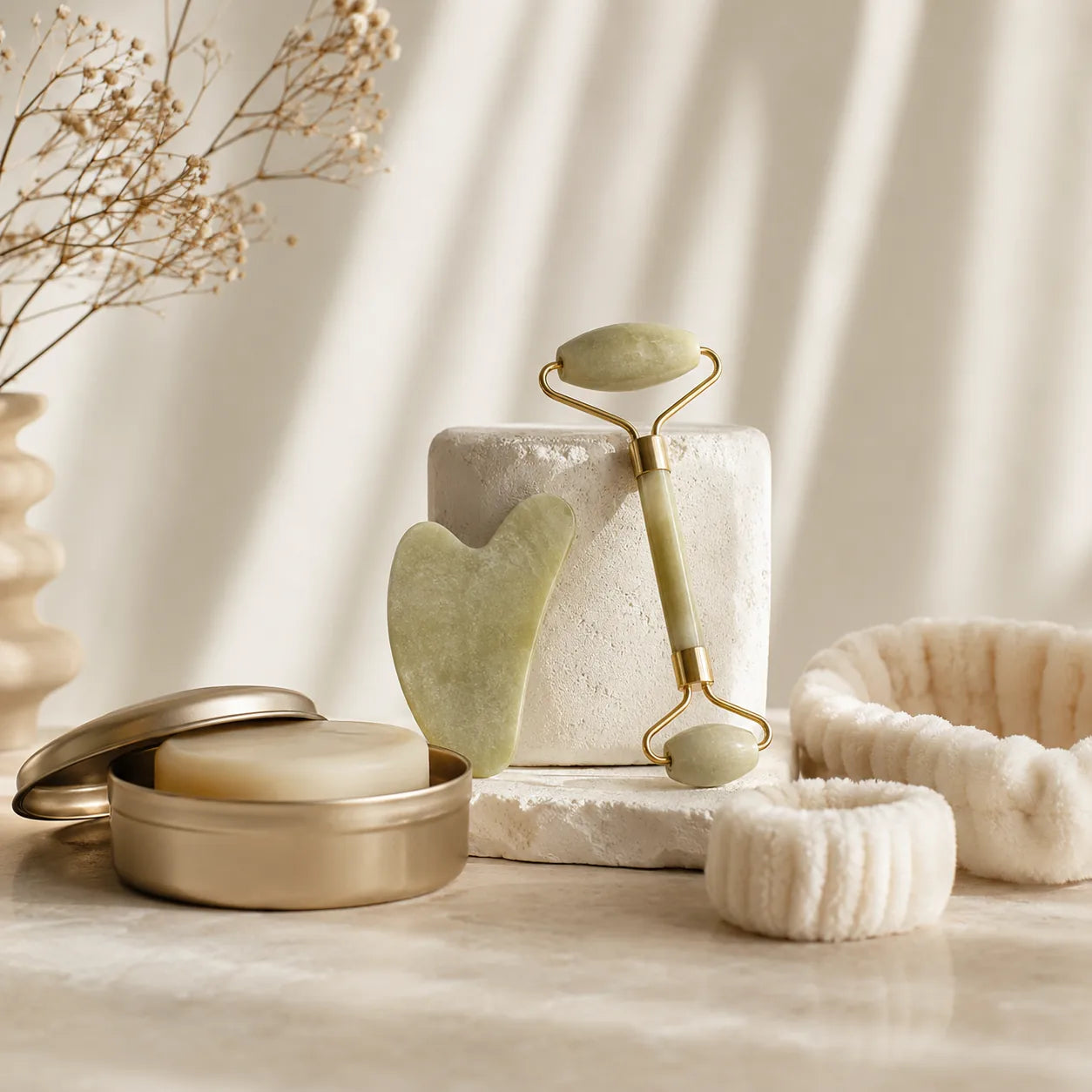 Mise en scène d’accessoires beauté avec gua sha, rouleau de massage, bandeau et boîte à savon